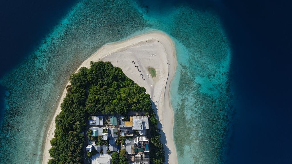 The tip of Ukulhas from directly above: a curve of white beach, dense palms, houses at the near end and reef running out into deep blue.